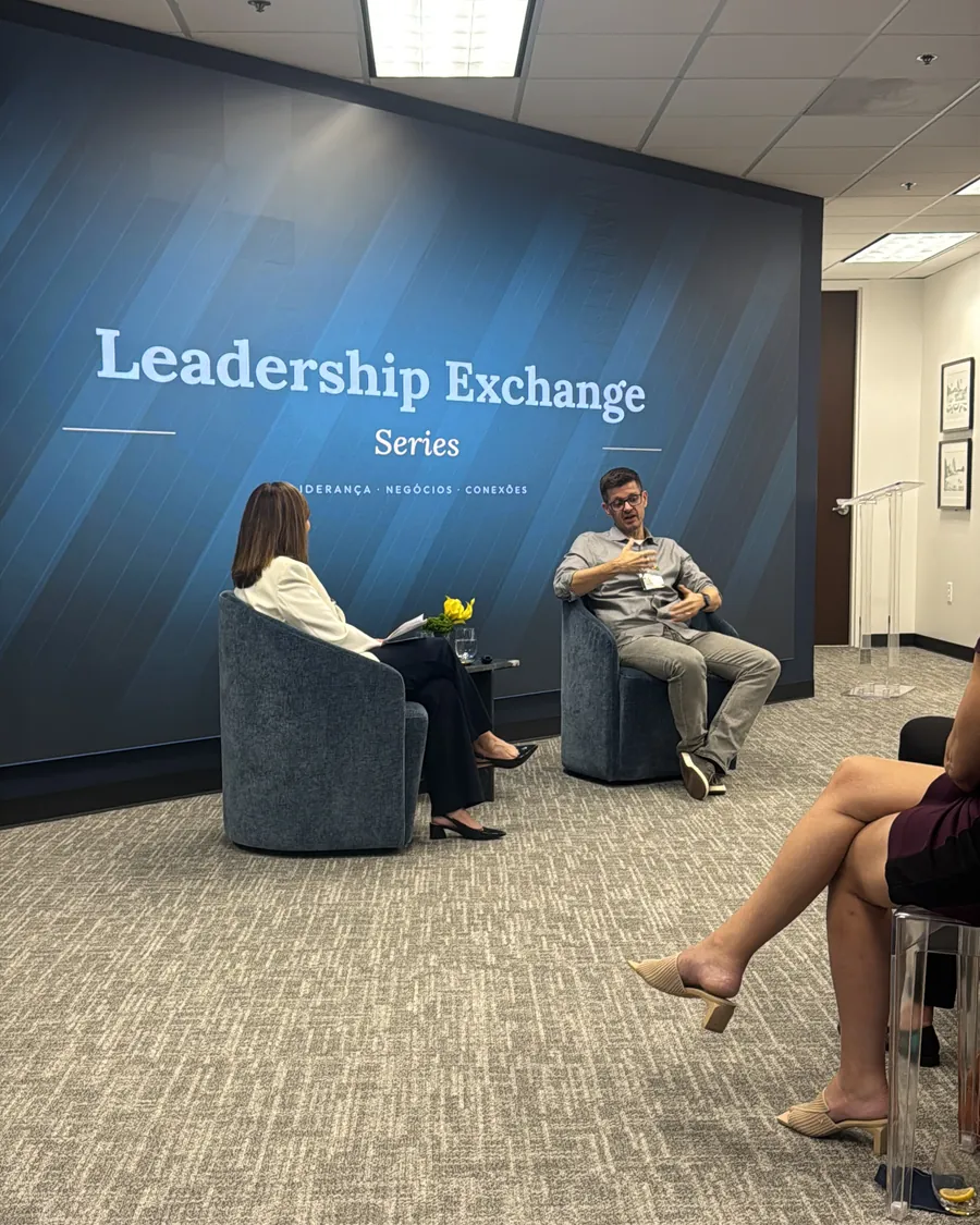 Cláudio Vilardo seated in conversation with the moderator in front of the Leadership Exchange Series wall
