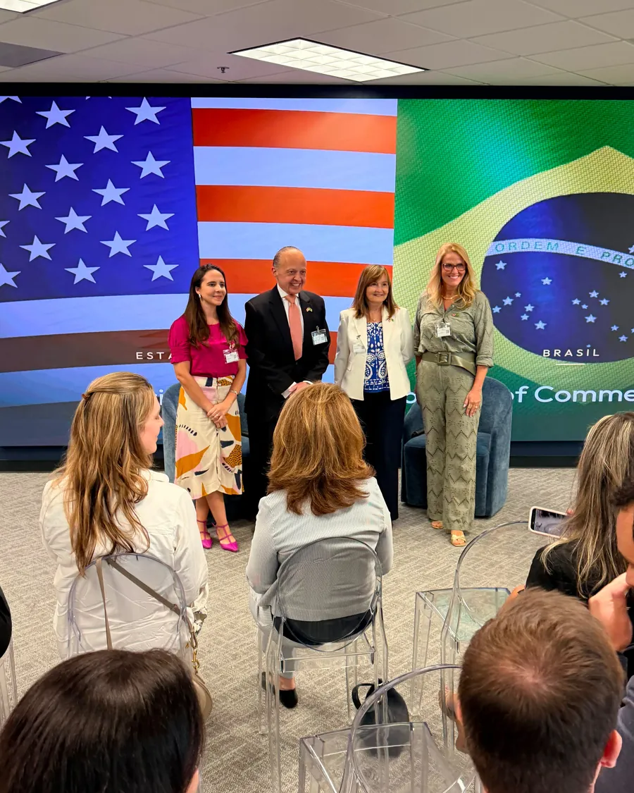 Four guests standing in front of the American and Brazilian flags on the screen, with the audience seated